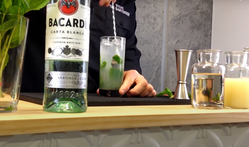 A glass of mojito garnished with a lime wedge and a mint sprig on a wooden table